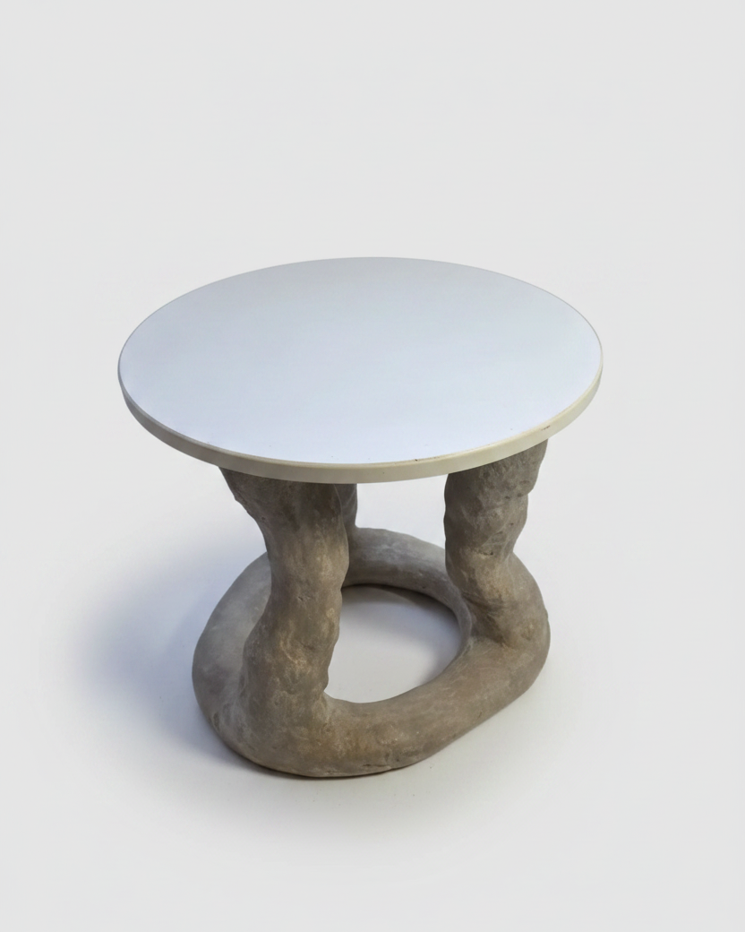 A modern sculptural side table featuring a round white top and a twisted, organic-shaped gray concrete base, photographed on a seamless light gray background.