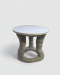 A small round side table with a smooth white top and a sculptural, tree-like gray concrete base, photographed against a plain off-white background.