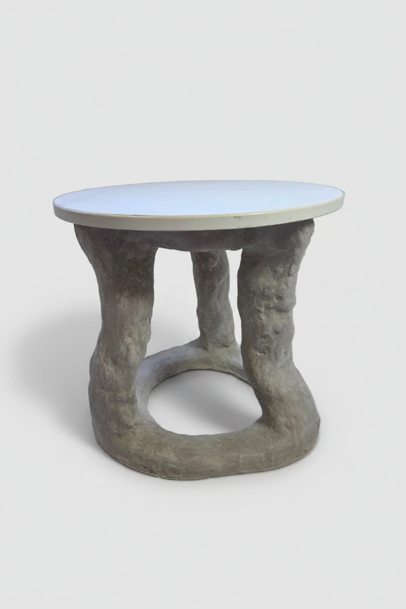 A sculptural side table with a round white top and a textured, organic-shaped gray concrete base, shown on a light gray background.