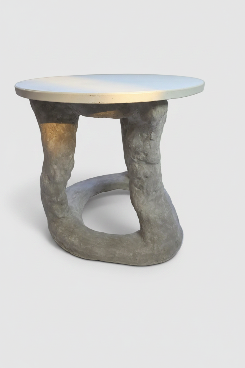 A sculptural side table with a round top and a twisted, tree-like gray concrete base, shown on a light gray background.
