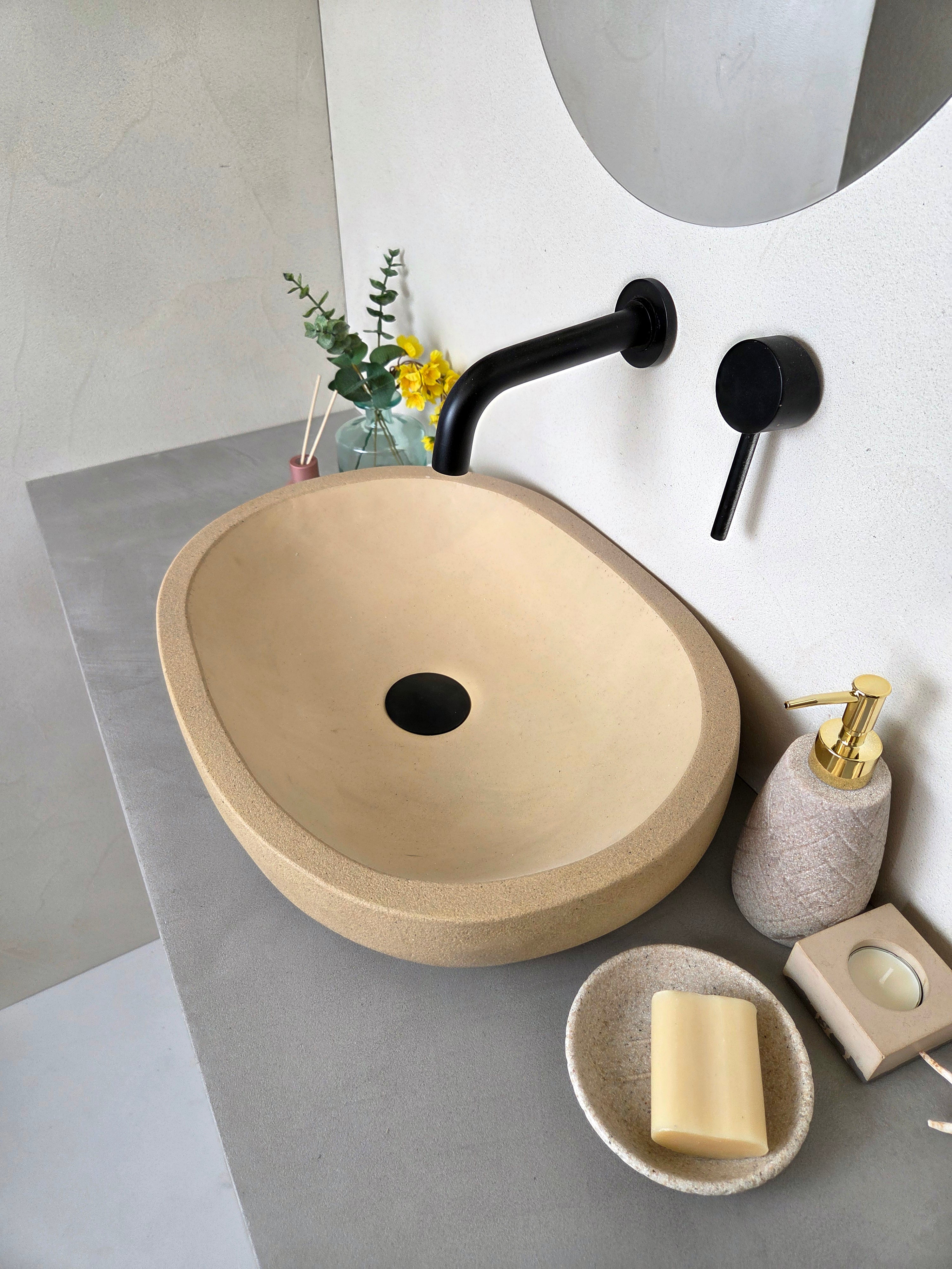 Beige concrete sink with black faucet on a gray countertop in a bathroom setting.