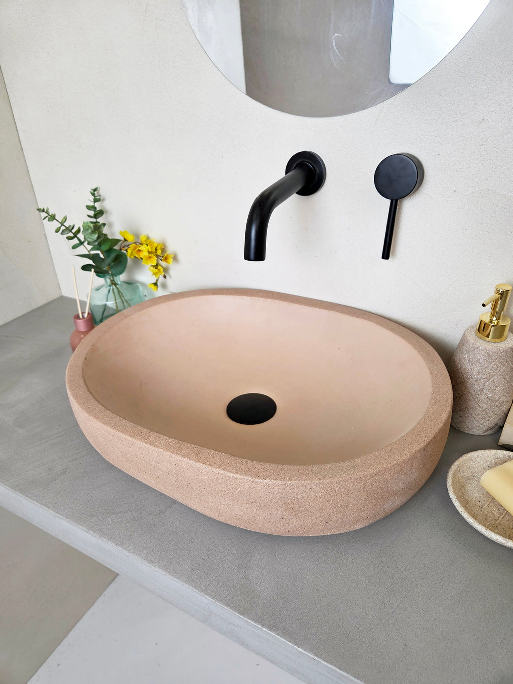 Oval bathroom concrete sink with beige stone basin, black faucet, and decorative elements.