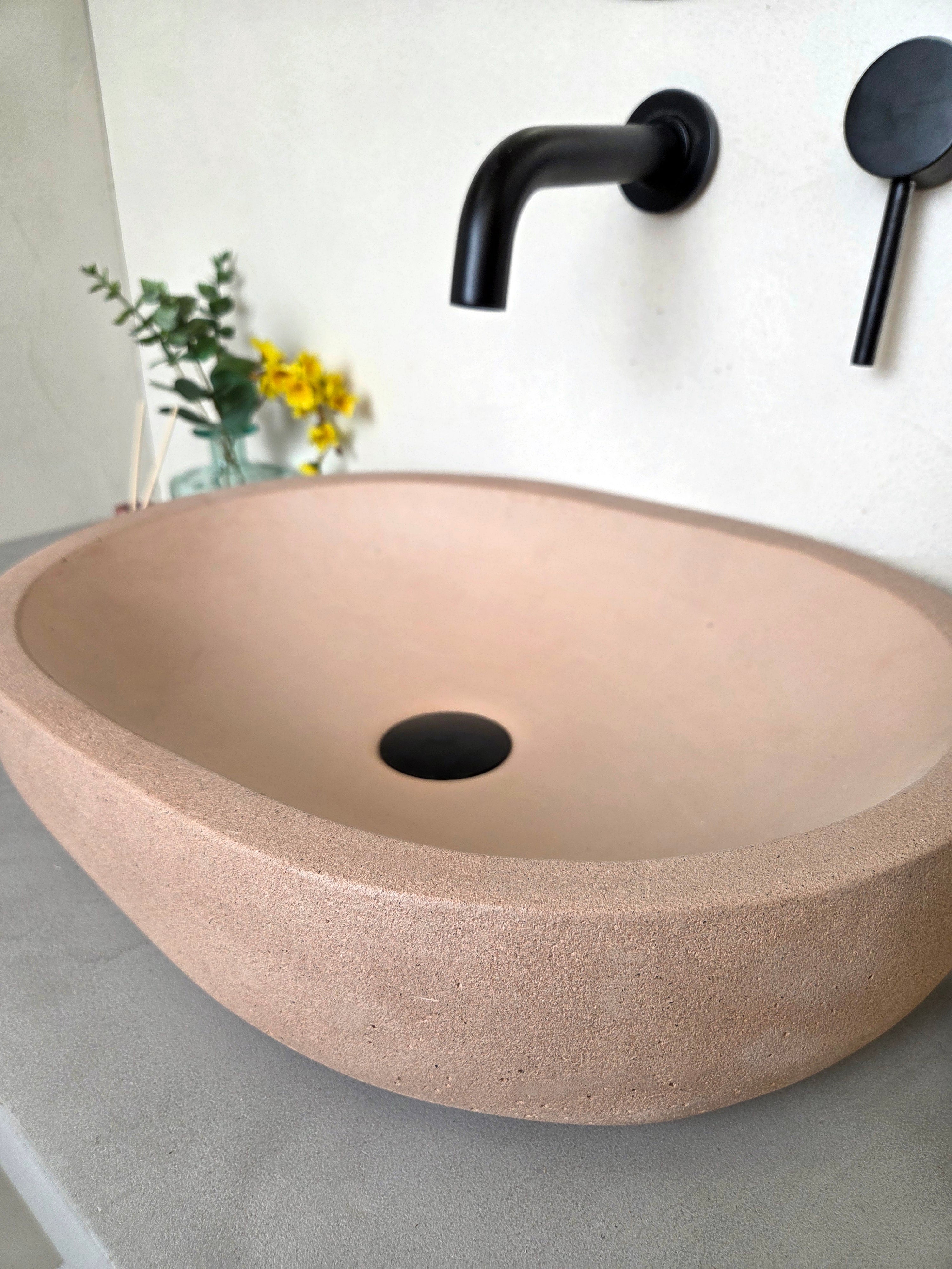 Pink concrete oval sink with black faucet and handle on a white wall.
