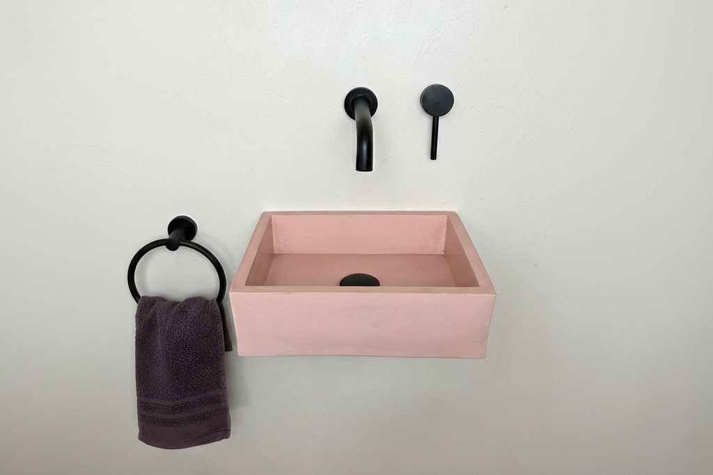 MINI concrete sink in pink with black faucet and towel holder on a white wall