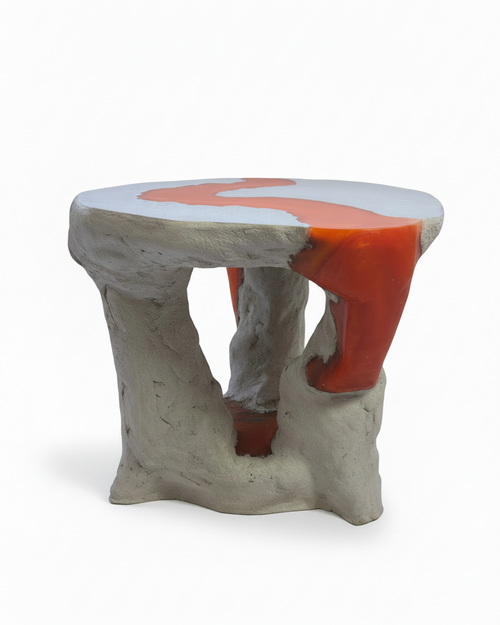 An abstract sculptural side table with a rough, concrete gray base and a smooth top featuring a red resin section flowing through the tabletop and leg Abstract design, shown on a clean white background.