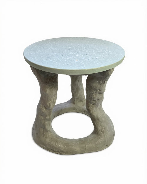 A round side table with a exposed aggregate light gray concrete top and a sculptural, tree-like concrete base in a weathered gray finish, shown on a white background.