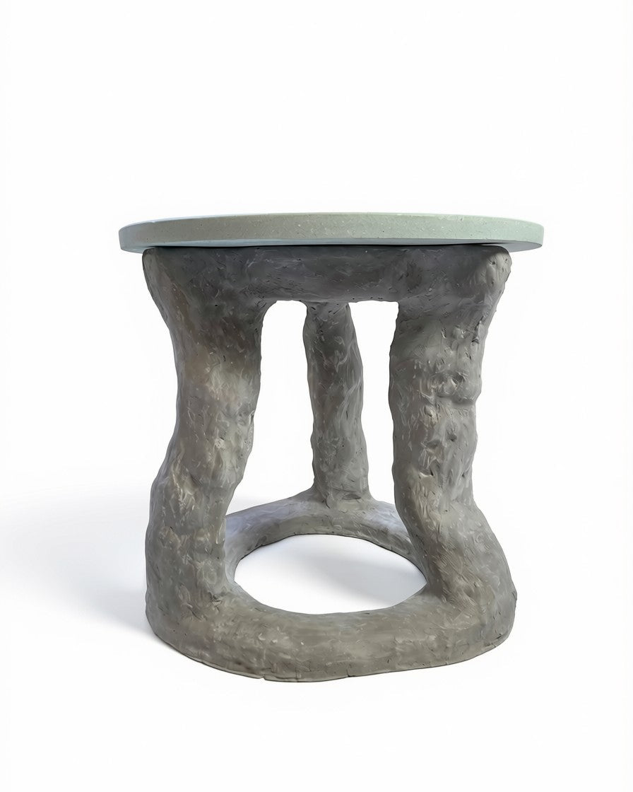 A rustic side table featuring a textured, tree-bark-like gray base and a smooth, light sage green circular tabletop, shown against a plain white background.