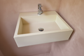 A modern rectangular wall-mounted concrete sink in a warm cream color with a polished chrome faucet, set against a textured dusty pink plaster wall.