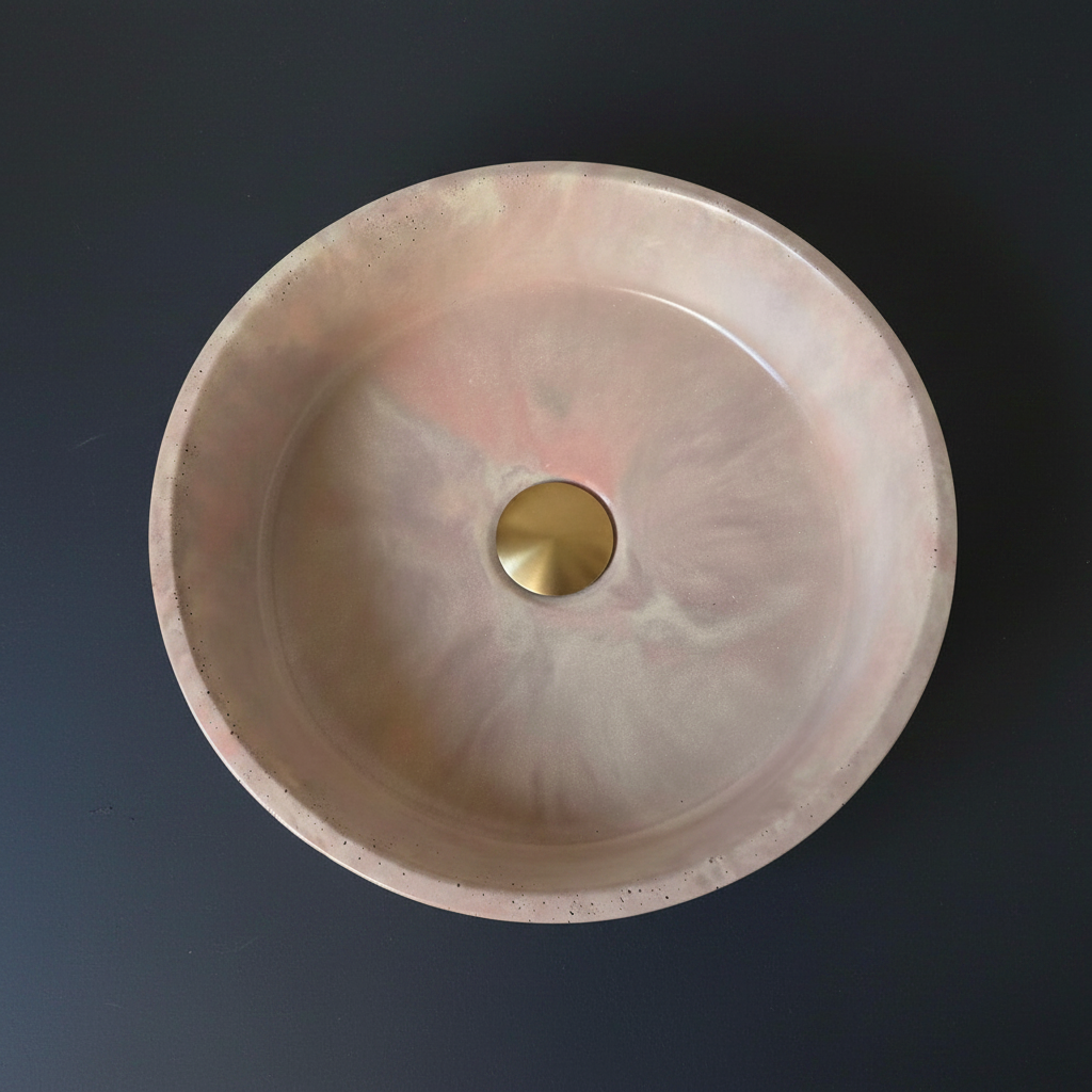 round concrete sink in marble effect finish pink and purple hues with brushed brass waste on black background