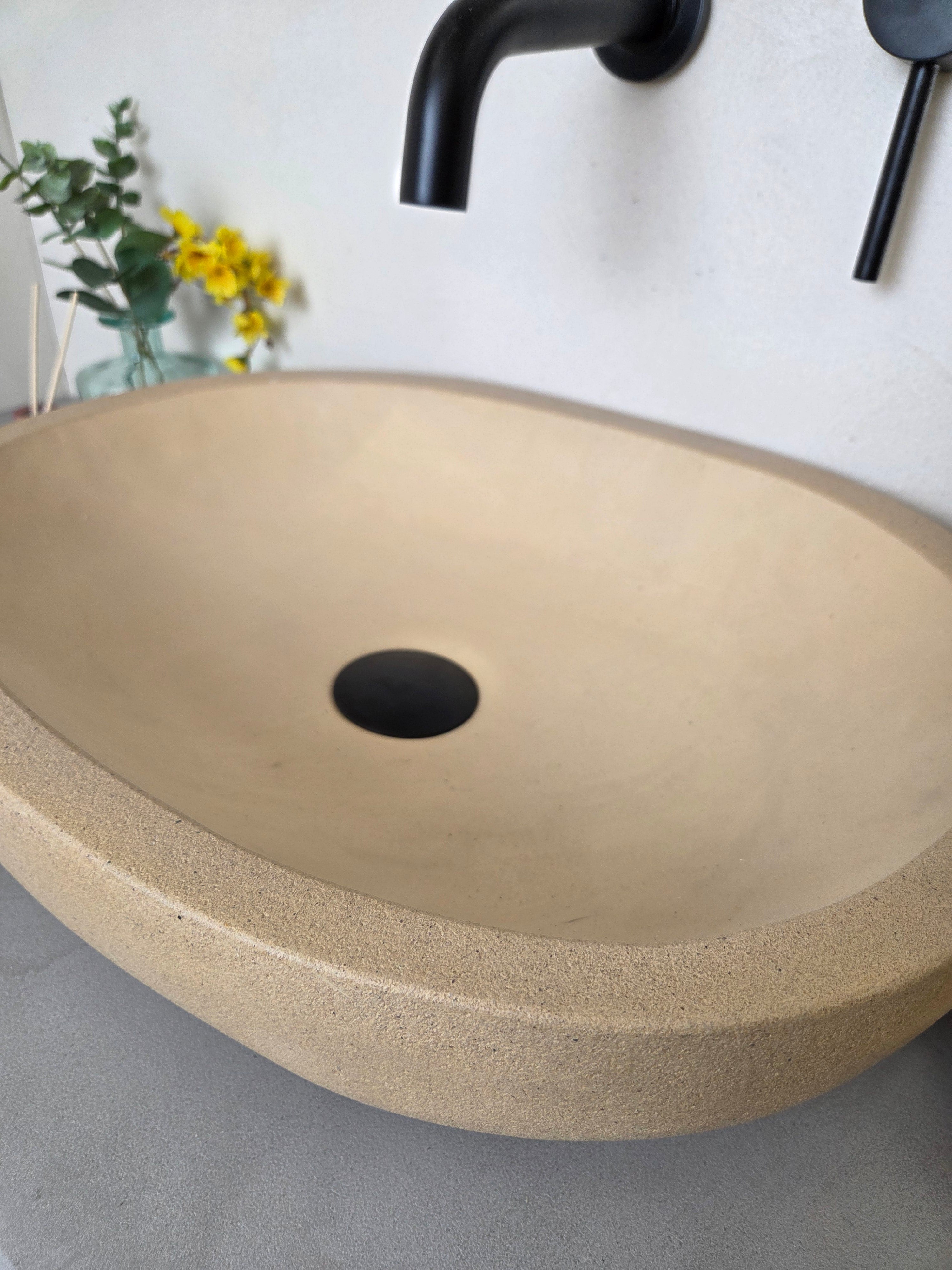 Beige concrete sink with black drain on a gray surface