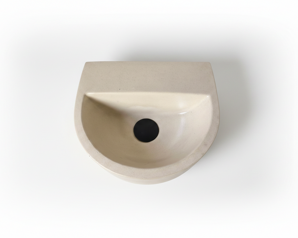 A minimalist, semi-circular wall-mounted concrete sink in a light beige finish, shown from a top-down perspective on a clean white background.