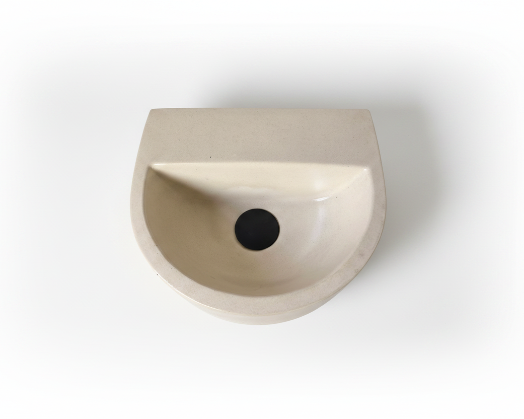 A minimalist, semi-circular wall-mounted concrete sink in a light beige finish, shown from a top-down perspective on a clean white background.
