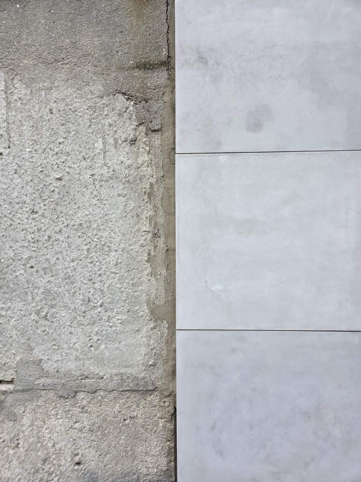 A close-up comparison of two wall finishes: a rough, textured gray concretewall on the left, and three large light gray concrete panels on the right.