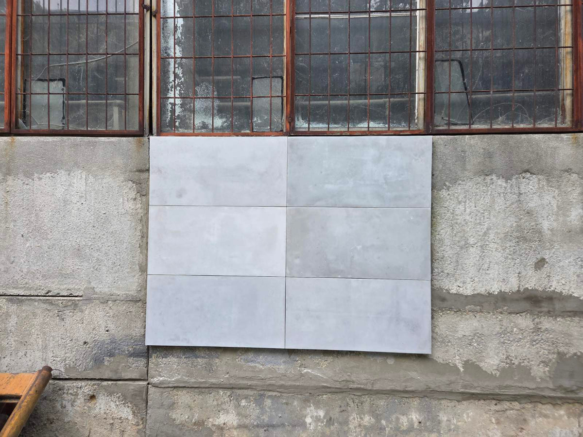 Six large square light gray concrete panels arranged in a 2x3 grid on a rough concrete wall beneath metal window frames.