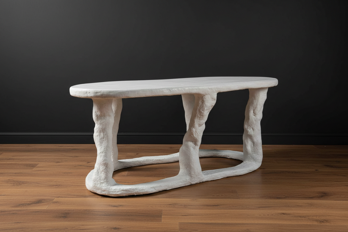 A sculptural, organic-shaped coffee table with a rough, textured white finish, set on a polished wooden floor against a dark charcoal wall.