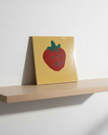 Wooden shelf with a concrete art piece featuring a red strawberry illustration on a yellow background.