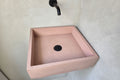 Pink square sink mounted on a white wall with a black faucet.