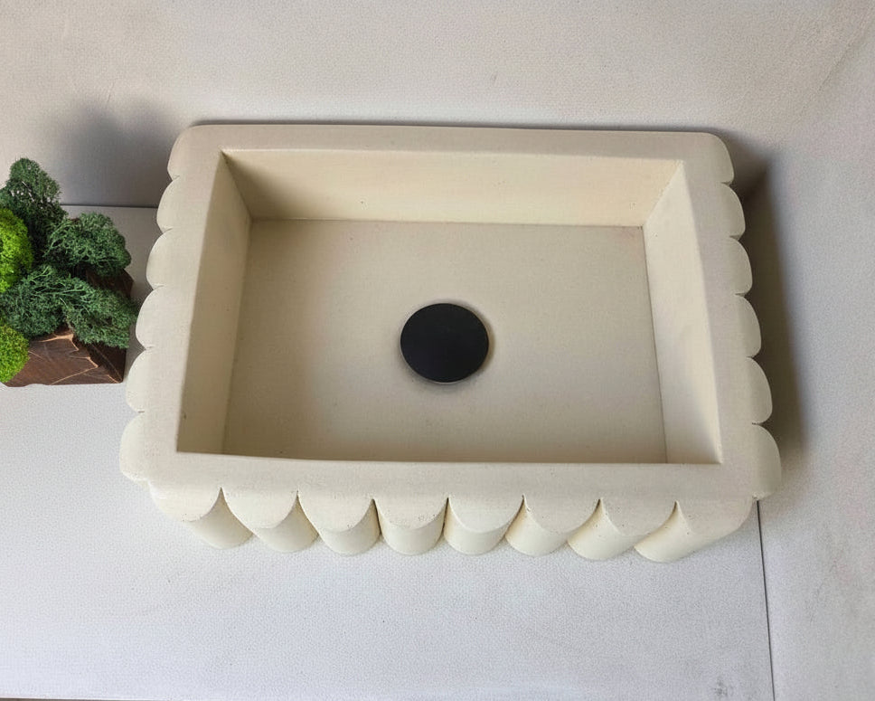 Concrete sink with scalloped edge on a microcement bathroom countertop, next to a plant.