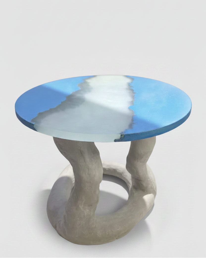 A modern round accent table with a blue and white abstract resin top and a sculptural twisted concrete base, shown on a light gray studio background.