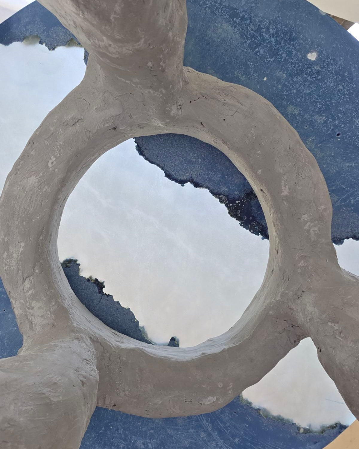 A close-up of a sculptural concrete table taken from the bottom and looking up through the partially translucent resin top. The top features cast concrete sections in bright blue colour. 