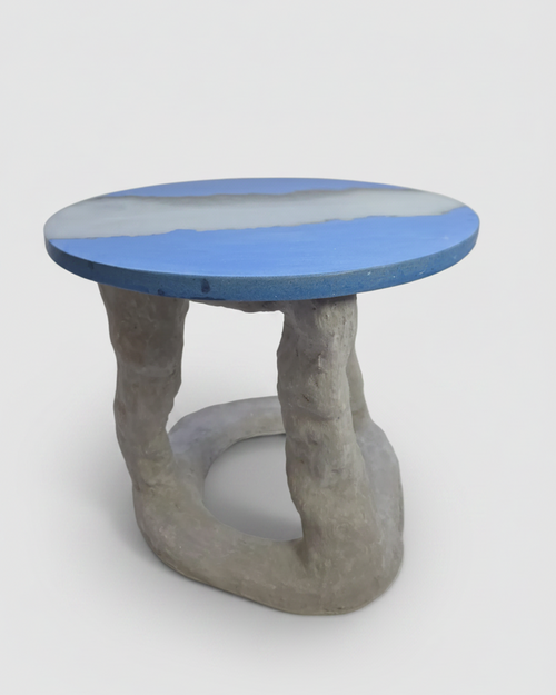 A sculptural side concrete table with a round blue concrete and translucent resin top and a twisted concrete base, shown on a light gray background.