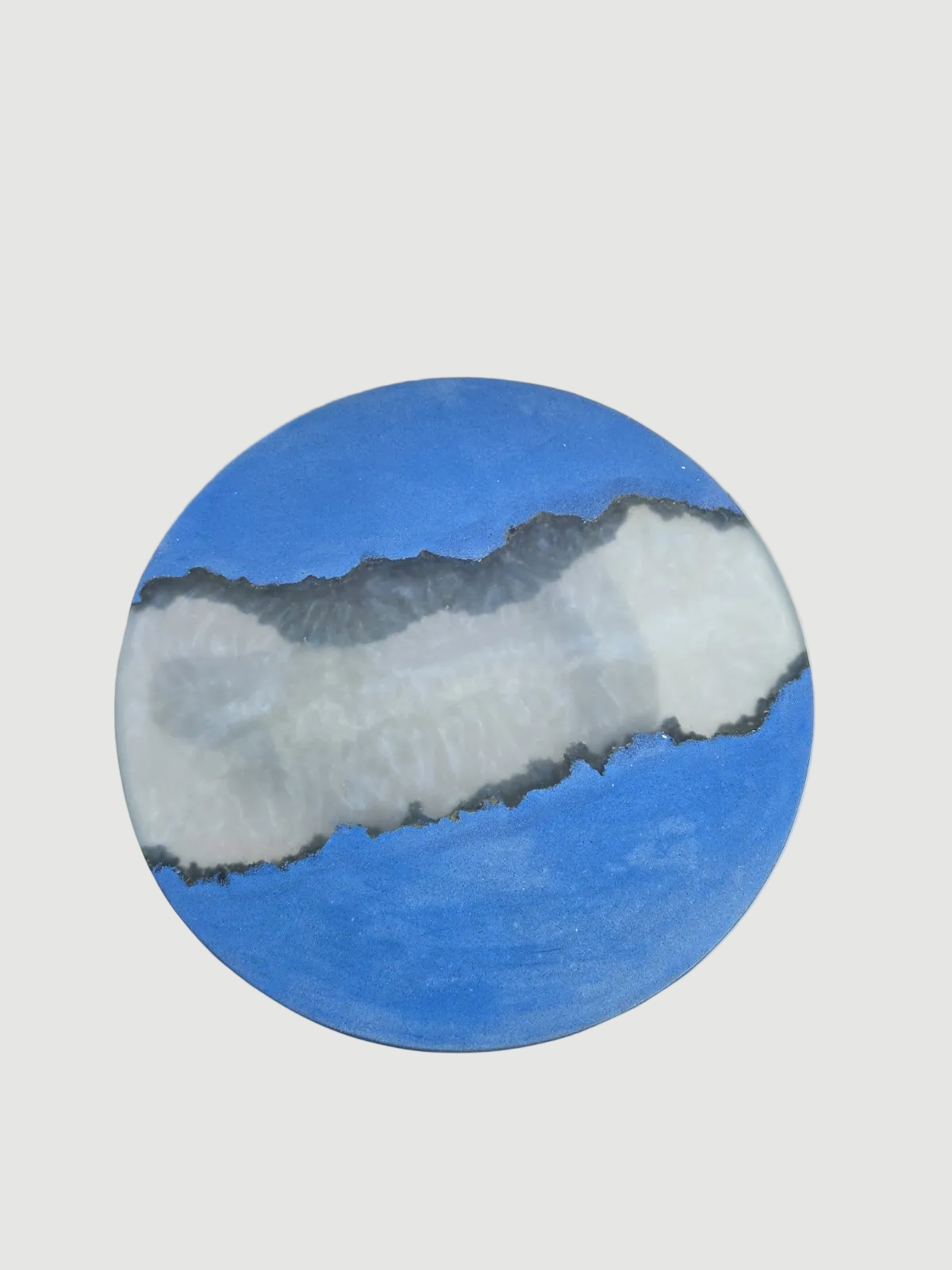 A circular concrete tabletop the looks like a stylized landscape painting of a white and gray mountain range under a bright blue sky, centered on a light gray background.