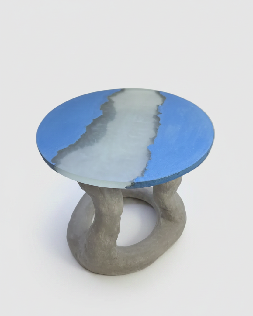 A small round side table with a blue and white agate-like patterned top and a sculptural gray concrete base, shown on a light gray background.