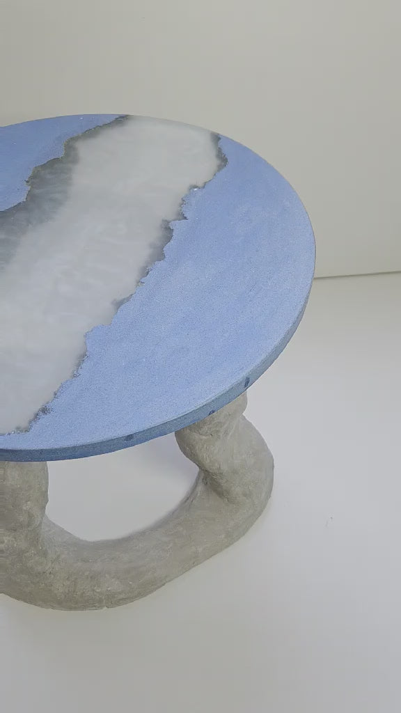 video of a sculptural coffee table featuring a hand shape concrete base and a cast concrete round top with an integrated resin section